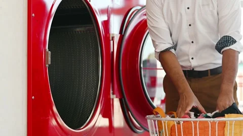 Drying clothes - a man putting clothes into a drying machine at the laundromat Stock Footage 252729274