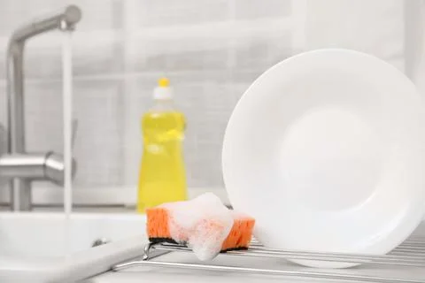 Drying rack with clean plate and soapy sponge in stylish kitchen Stock Photos