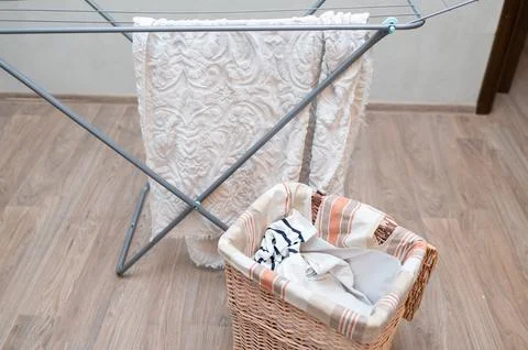 Drying rack with hanging laundry and laundry basket nearby at home Stock Photos