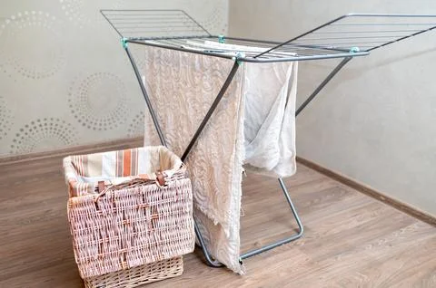 Drying rack with hanging laundry and laundry basket nearby at home Stock Photos