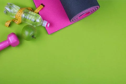 Dumbbells, apple, bootle, mat and measuring tape on green background Stock Photos