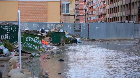 Dump garbage bags lying next to trash cans and puddle on broken road Stock Footage 101540336