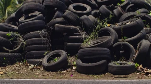 A dump of old tires and bikes and cars pass in front of them, the old generation Stock Footage 256064739