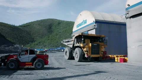 A dump truck pulls away from an industrial repair garage near an open pit mine Stock Footage 221044309