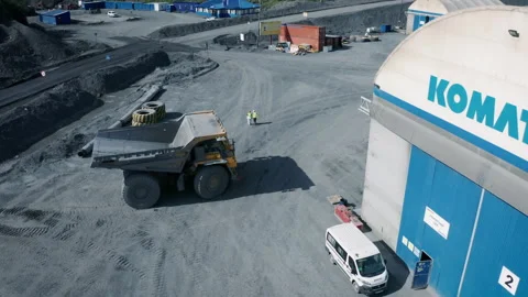 A  dump truck pulls away from an industrial repair garage near an open pit mine. Stock Footage 221045116