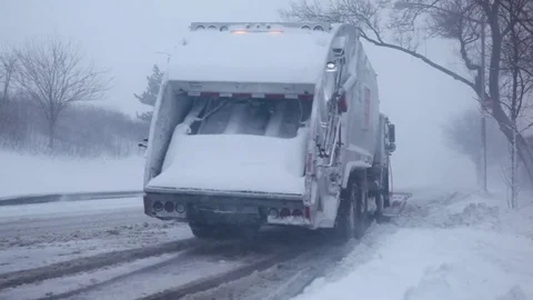 Dump truck with snow plow pulling away from curb in snow storm Stock Footage 73677366