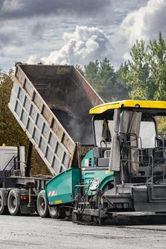 A dump truck is unloading material into a paving machine at a construction .. Photos