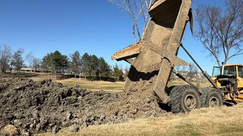 Dump Truck Unloading Soil on Grassy Worksite Under Clear Sky Stock-Fotos