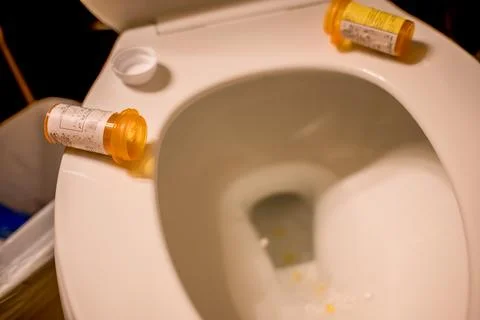 Dumping medication pills from a plastic bottle into an open toilet Foto stock