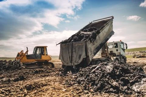 Dumping truck unloading garbage at dumping site. Industrial bulldozer, excavator Stock Photos