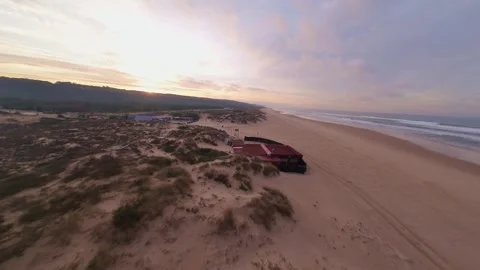 Dune-covered coastline at dawn, featuring modern buildings near shore Stock Footage 344542323