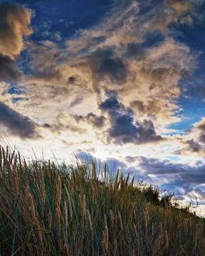 Dune under a dramatic sky with clouds and sunshine in the background on the b Stock Photos