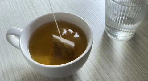 Dunking a tea bag in a hot beverage next to a glass of water Vídeo Stock 338186439