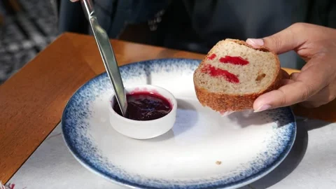 During breakfast, the individual spreads jam on bread to add a sweet touch to Stock Footage 279290012