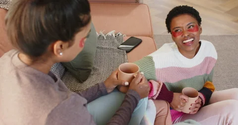 During chat, diverse friends with under-eye patches at home sipping mugs and Stock Footage 314045715