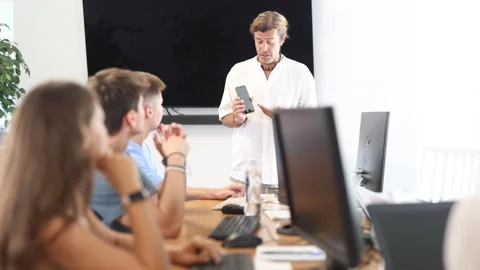 During computer courses, male teacher with mobile phone explains to listeners Stock Footage 313097731