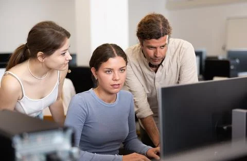 During computer lesson, two companions help girl student complete difficult task Foto stock