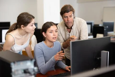 During computer lesson, two companions help girl student complete difficult task Foto stock