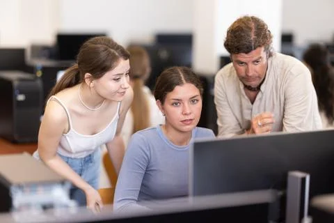 During computer lesson, two companions help girl student complete difficult task Stock Photos