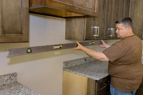 During the installation of new kitchen cabinets, the worker hangs a level to Stock Photos