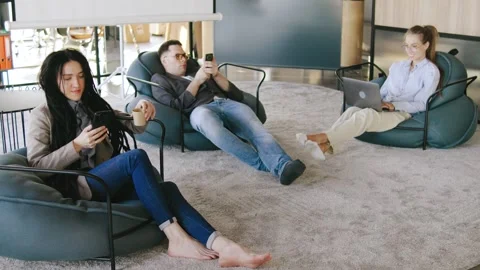 During a lunch break at the office, workers sit in the lounge area, checking Stock Footage 292640806
