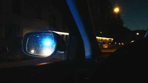 During a night traffic stop, a driver sees police car lights flashing in their Stock Footage 277953535