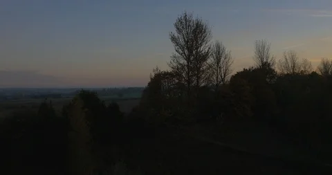 Dusk, aerial movement through trees to reveal sunset countryside Stock Footage 102397567
