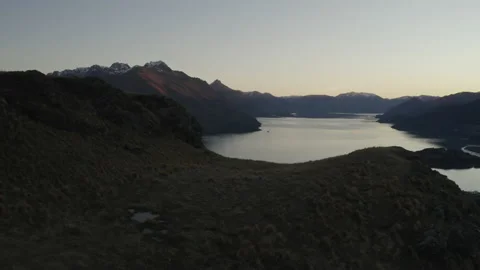 Dusk drone over foreground hill to show still lake and mountains Stock Footage 159049499