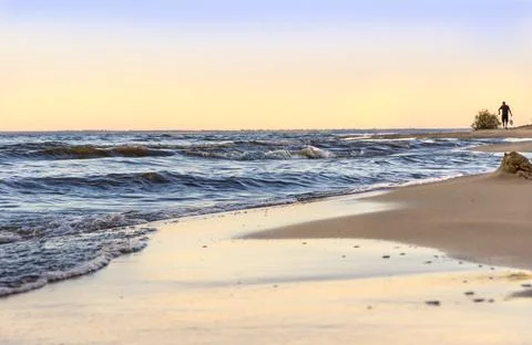 At dusk, low waves roll over the sandy shore, in the distance a person is Foto stock