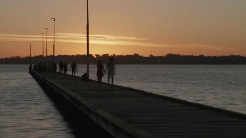 Dusk over river viewed along jetty. Backlit time lapse as people stroll along Video stock 151658803