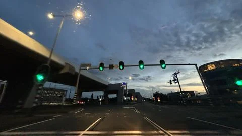 Dusk roadway view through windshield with green traffic lights, urban Stock Photos