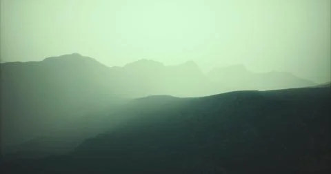 Dusk settles over the rugged mountain landscape shrouded in mist 스톡 일러스트