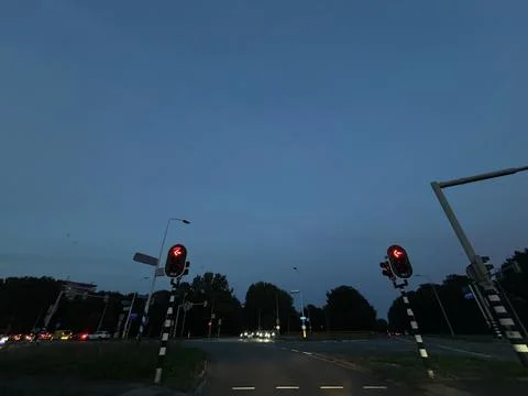 Dusk traffic intersection with glowing red signals, curving roadway, distant Stock Photos