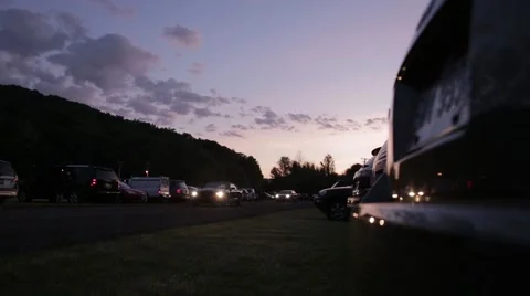 Dusk view of cars pulling into a gravel parking lot, low angle Stock Footage