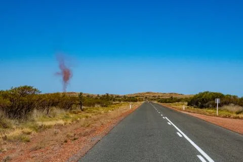 Dust devil besides dark road leading through red sanded Australian landscape  Stock Photos