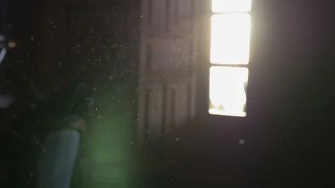 Dust floating in the air of a dark room with an open window and sunglare