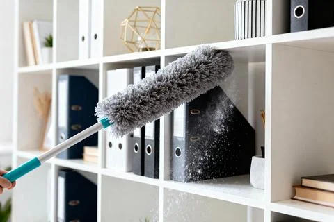 Dusting a shelf with a duster, cleaning home or office space Stock Photos
