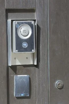 Dusty modern silver intercom and keyless entry system on a dark wooden door. Stock Photos