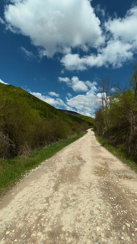 Dusty path winds through green hills under blue sky. Tupavica area, Vertical Stock-Footage 335947539