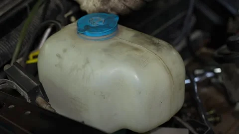 A dusty plastic windshield washer fluid reservoir tank with a blue flip cap i Stock Footage 345108926
