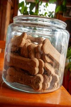 Dutch-angle of bone-shaped dog biscuits in an open glass jar on a wooden table Foto stock