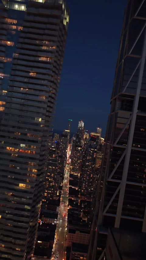 Dutch angle cinematic flight between illuminated skyscrapers and apartment build Video stock 335226097