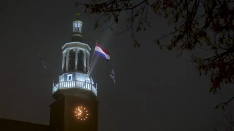 Dutch flag waving on an illuminated clock tower at night Video stock 323384668