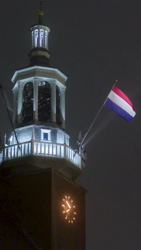 Dutch flag waving on an illuminated clock tower at night Video stock 327109784