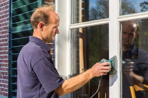 Dutch painter scours window frame with sander Stock Photos