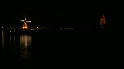 Dutch windmill, with lights at night, and a church tower with clock Stock Footage 13363039