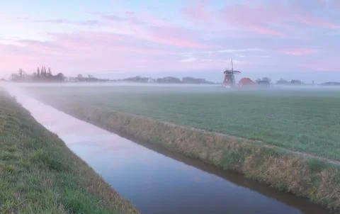 Dutch windmill by river in mist Stock Photos