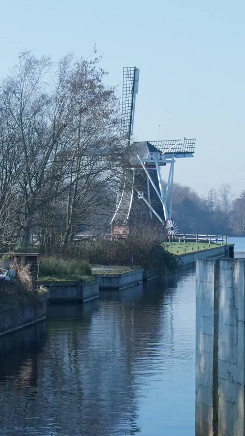Dutch windmill standing next to a tranquil canal Stock Footage 334424427