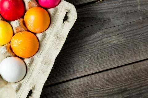 Dyed easter eggs in cardboard box on wooden background. Stock Photos