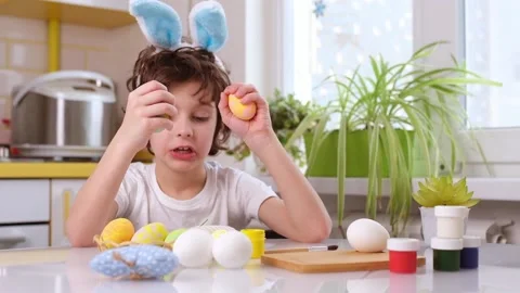 Dyeing Easter eggs. curly boy dressed in white Tshirt and blue bunny ears paints Stock Footage 172384212